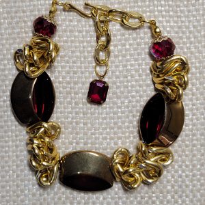 A bold, handmade bracelet featuring chunky gold chains and three large, faceted oval beads in a deep, vibrant red.